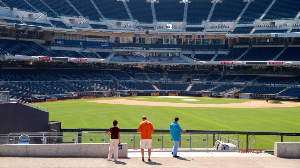 Ein Baseballstadion mit leeren Tribünen, einem Baseballfeld und drei Personen in der Nähe des Zauns.