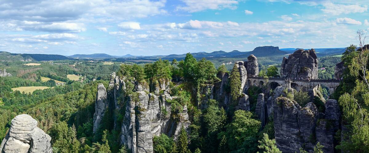 A landscape with tall rock formations, a bridge, and a valley with trees and distant hills.