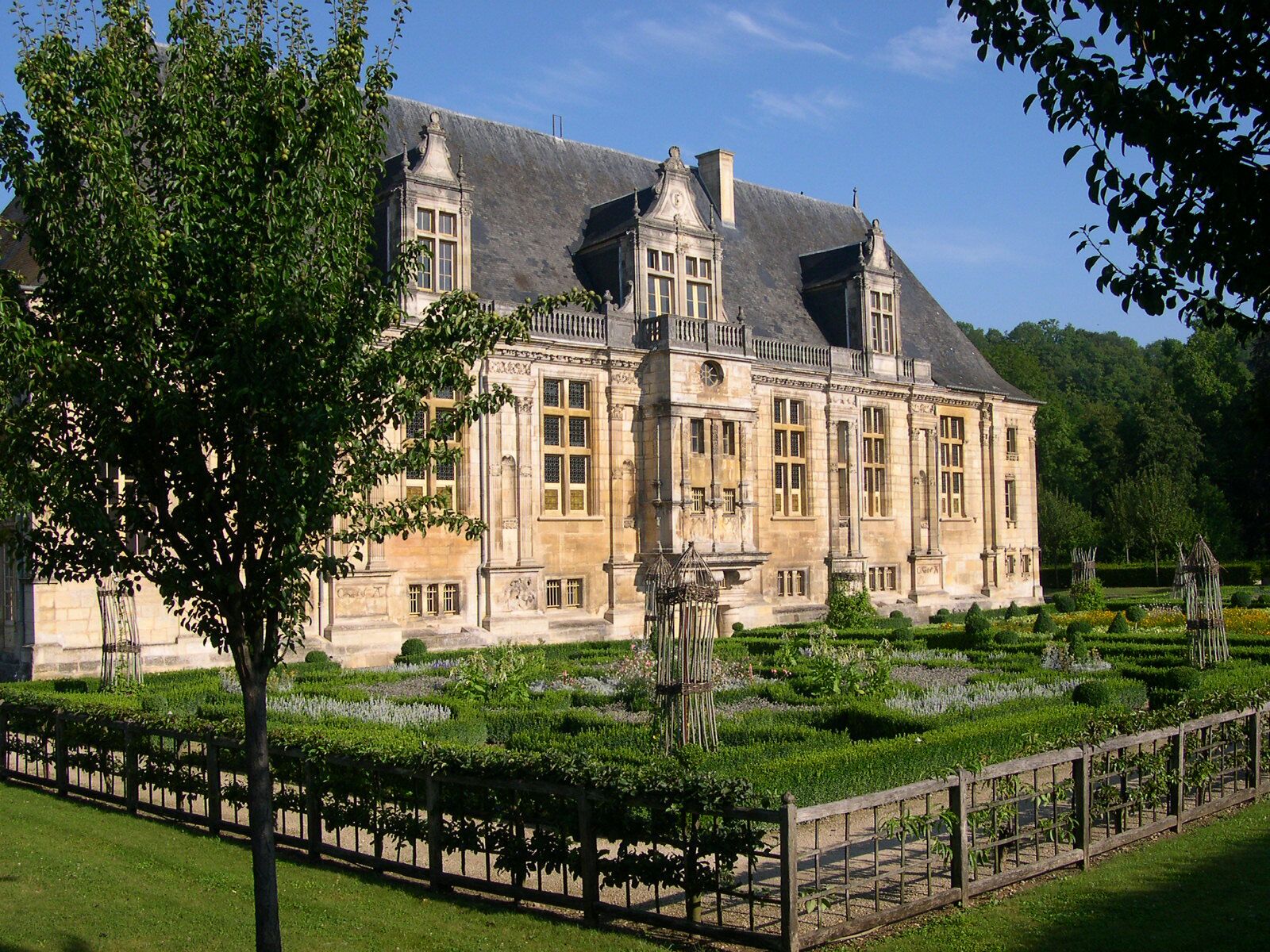 A large, historic building with a symmetrical facade, surrounded by well-manicured gardens and a clear blue sky.