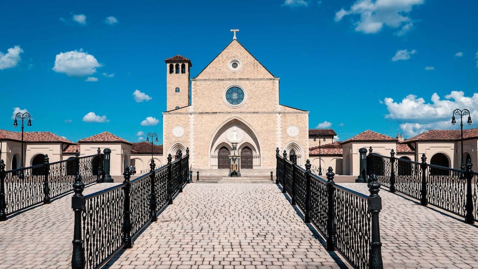 A historic church with a prominent clock tower and arched entrance, surrounded by a cobblestone courtyard and black iron fencing.