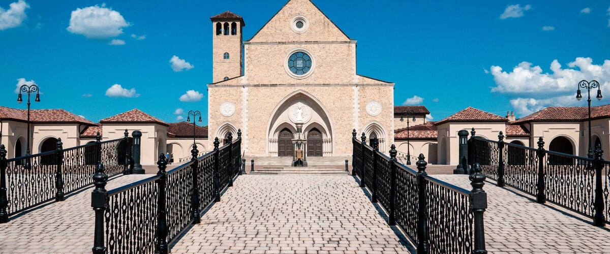 A historic church with a prominent clock tower and arched entrance, surrounded by a cobblestone courtyard and black iron fencing.