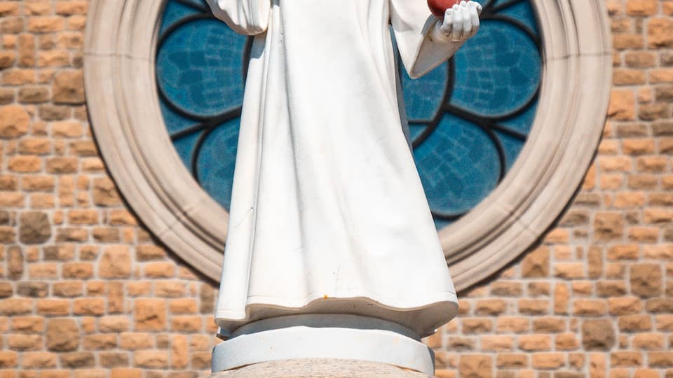 A statue of a child holding a red apple in front of a brick wall with a circular stained glass window.