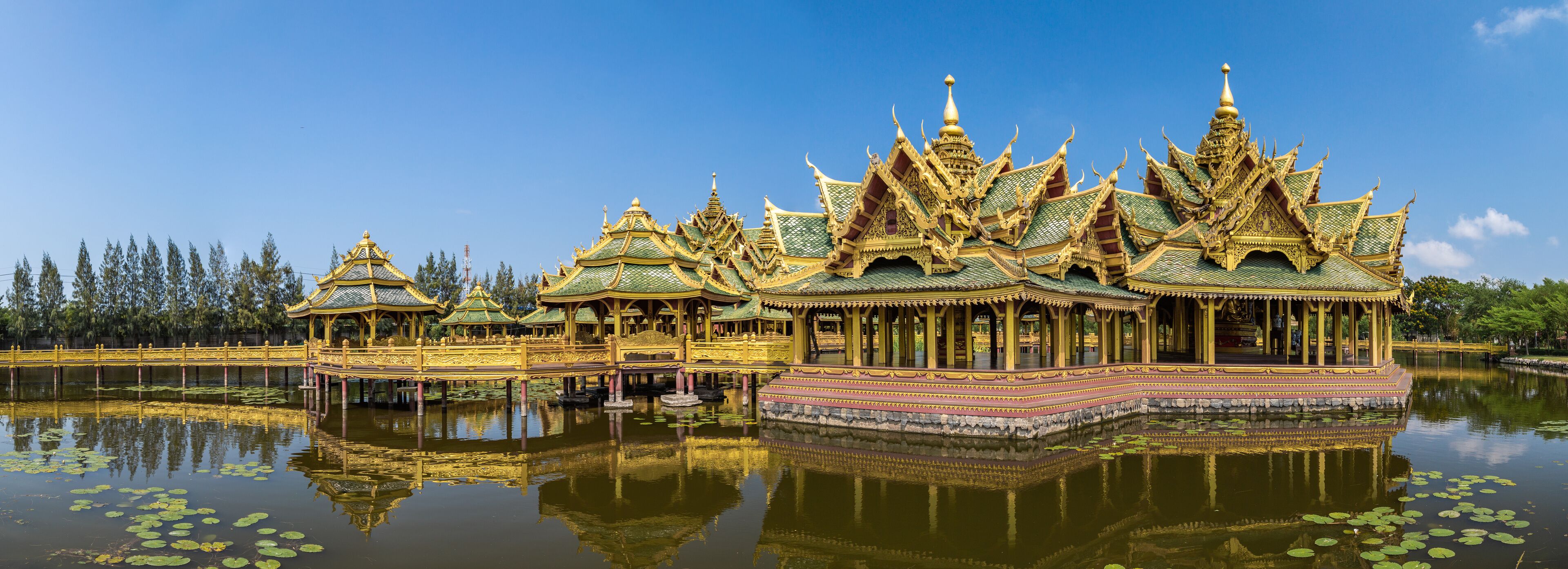 A traditional Thai temple with ornate golden roofs and a reflection in the water.