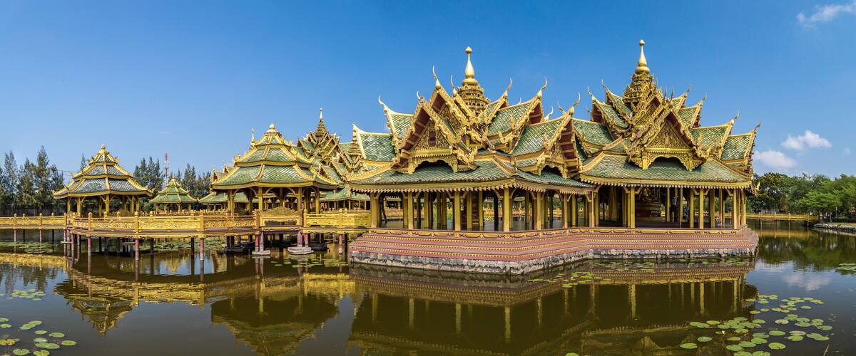 A traditional Thai temple with ornate golden roofs and a reflection in the water.