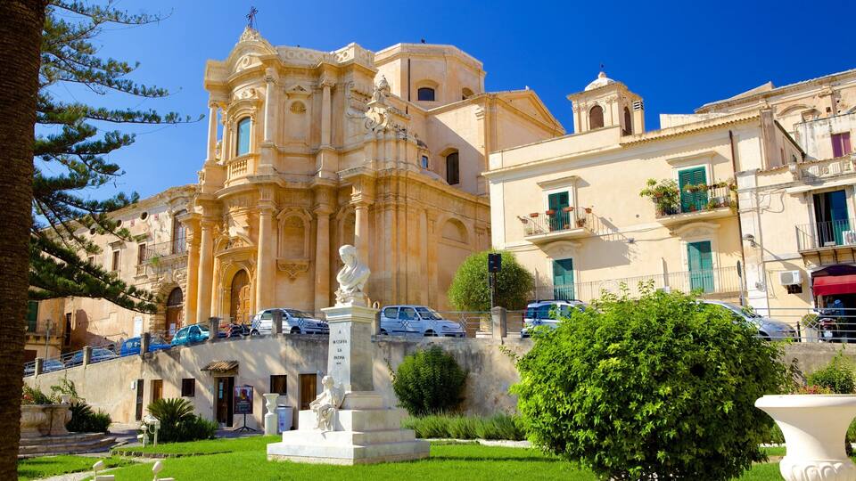 A historic church with ornate architecture, a statue in the foreground, and a well-maintained garden.