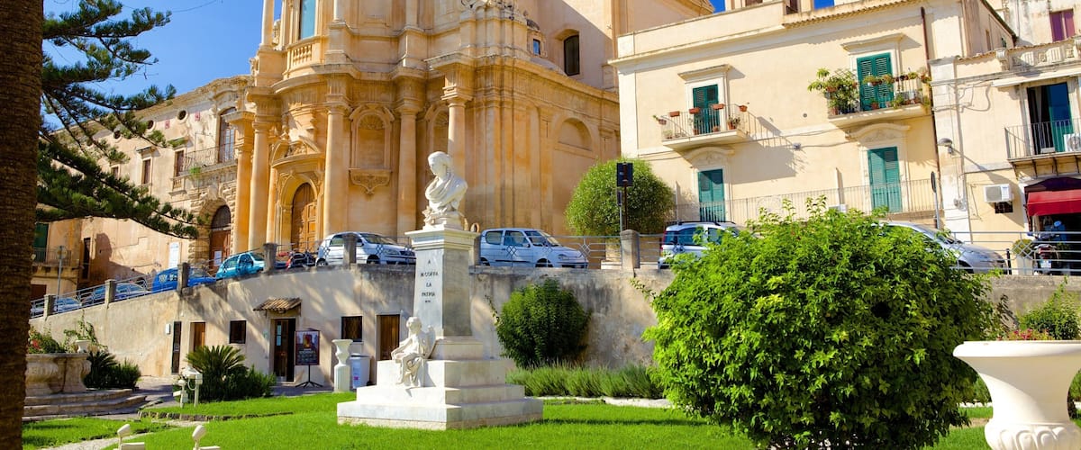 A historic church with ornate architecture, a statue in the foreground, and a well-maintained garden.