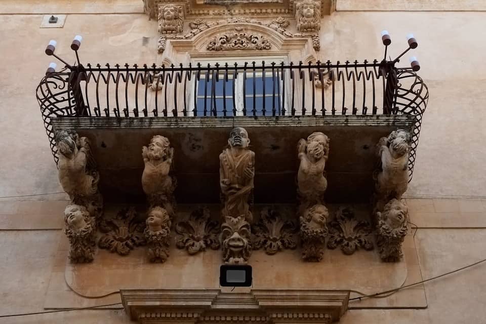A balcony with ornate lion sculptures and a wrought iron railing.