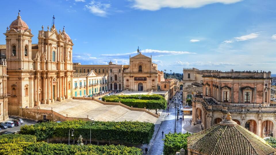 A historic plaza with a prominent church, a fountain, and surrounding buildings.
