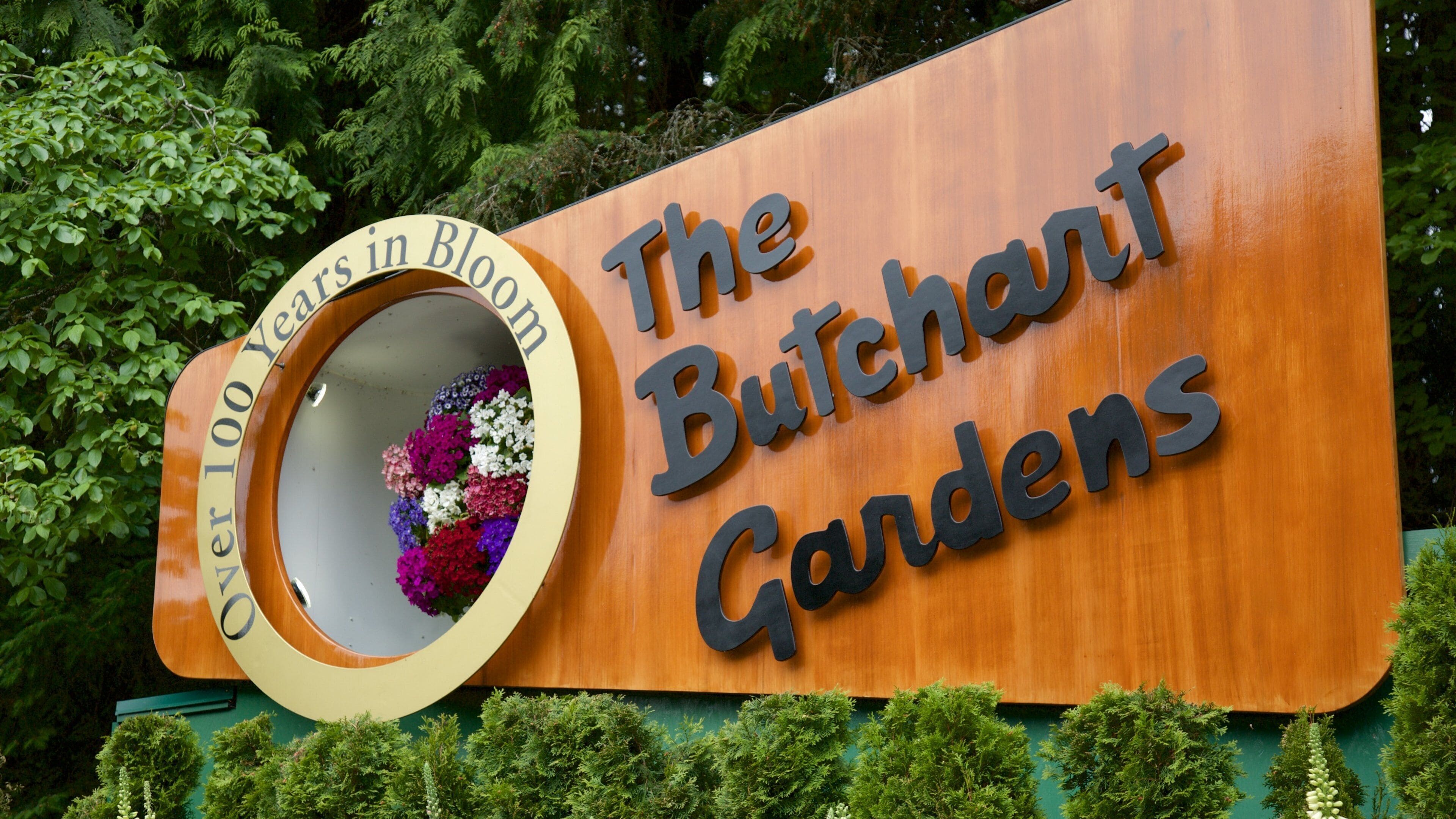A sign for The Butchart Gardens with a circular mirror reflecting colorful flowers.