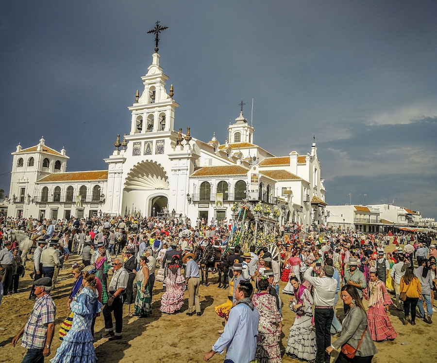 Una multitud se reunió frente a una iglesia blanca con un campanario y una cruz en la parte superior.