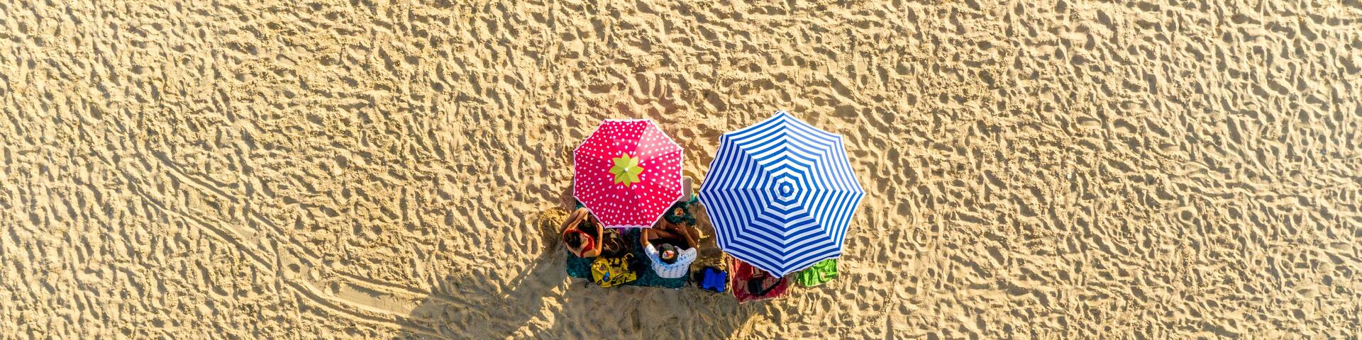 Aerial view of two umbrellas on the beach and people seating on their towels on Playa de Cuesta Maneli near Huelva, Spain.