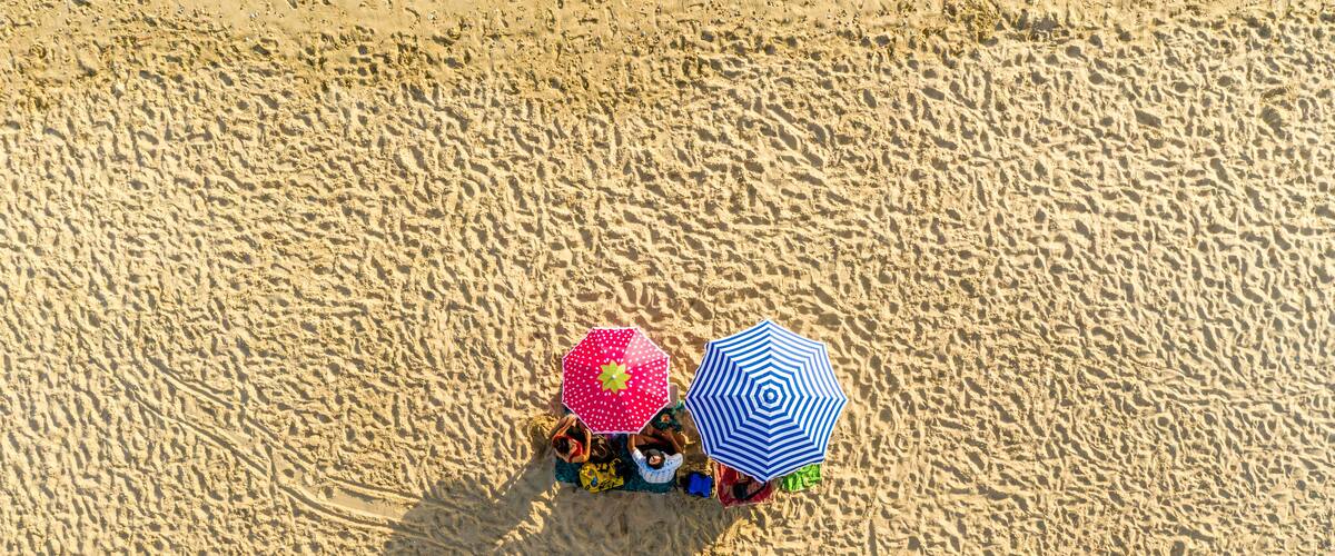 A sandy beach with two umbrellas and beach chairs.