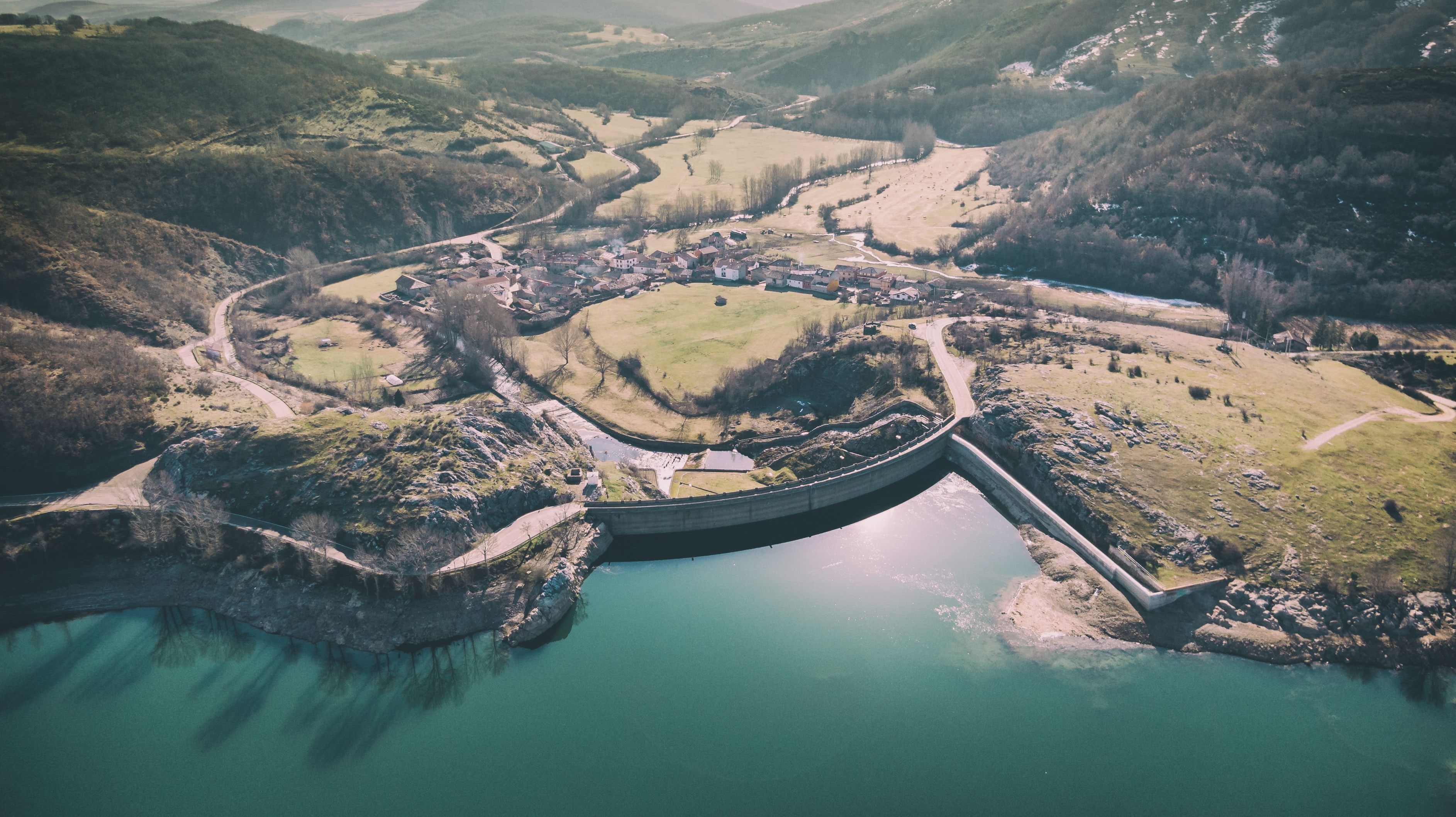 A dam, a river, and a village surrounded by hills.