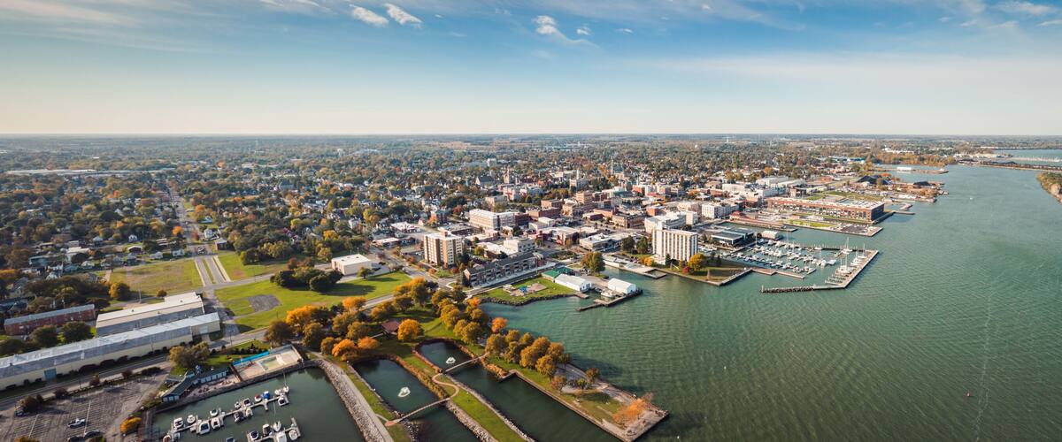 Incredible aerial city skyline panorama photograph of Sandusky, Ohio from the shoreline of the bay in Lake Erie with parks and harbors seen below on a sunny day.