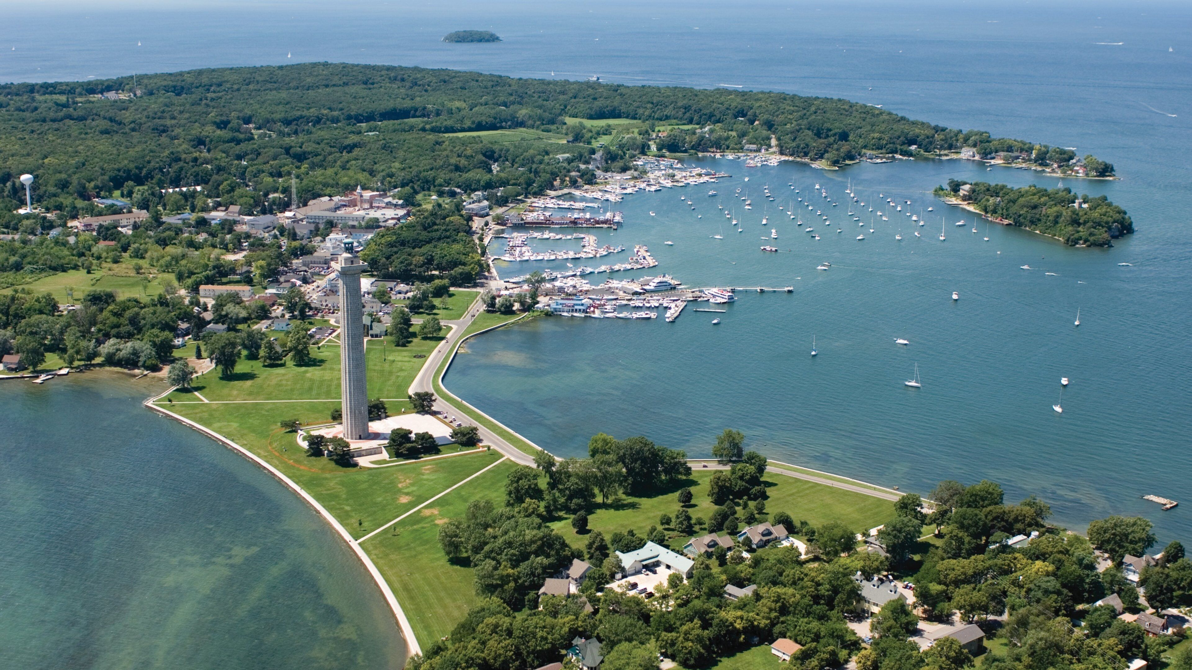 An aerial view of a coastal town with a prominent lighthouse, marina, and lush greenery.
