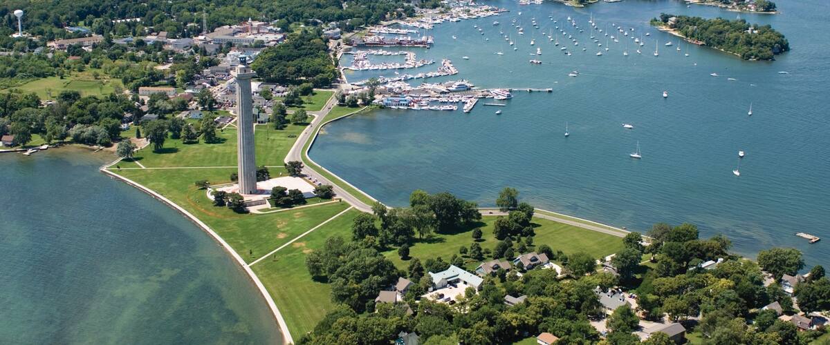 An aerial view of a coastal town with a prominent lighthouse, marina, and lush greenery.