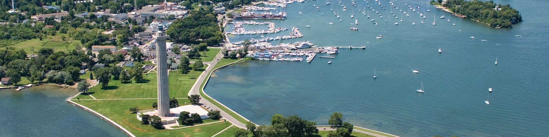 An aerial view of a coastal town with a prominent lighthouse, marina, and lush greenery.