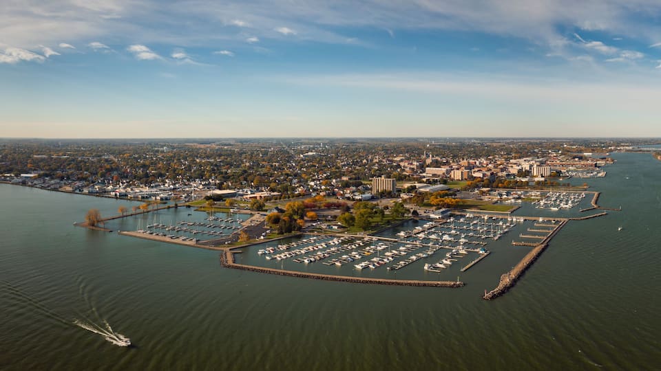 An aerial view of a marina with boats docked, surrounded by a cityscape and a large body of water.