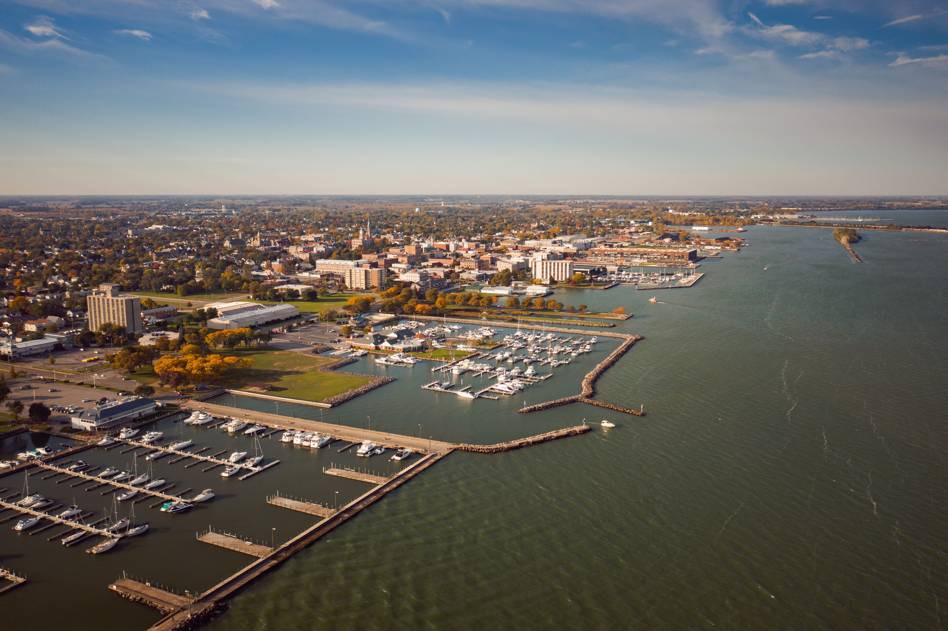 An aerial view of a marina with boats docked, a cityscape in the background, and a river.