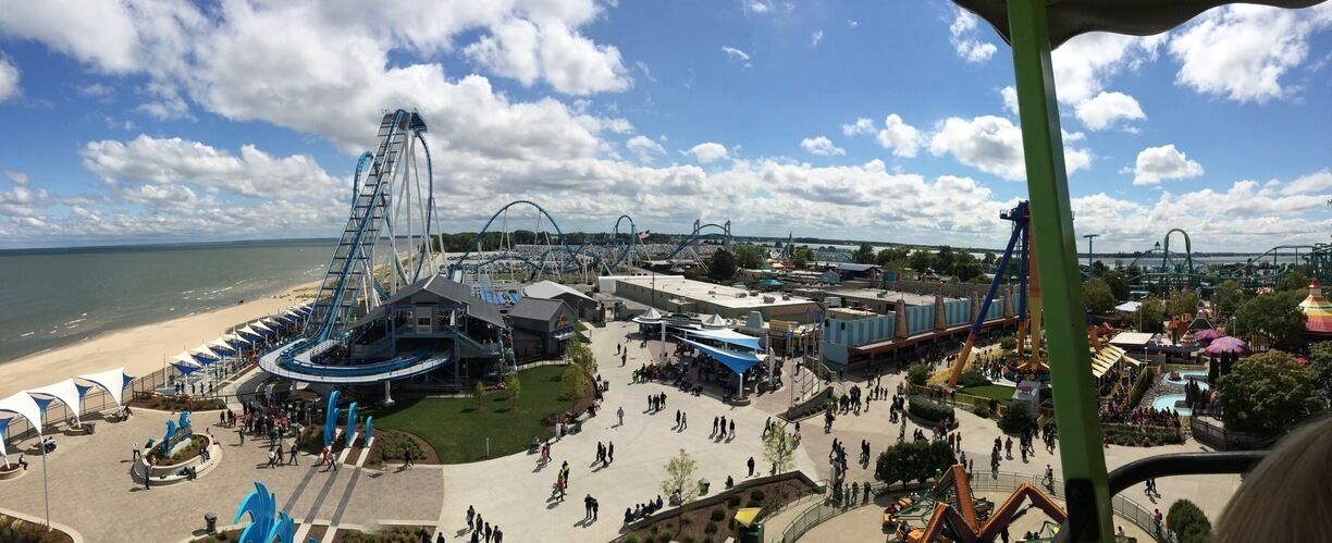 A theme park with a large Ferris wheel, roller coasters, and a beach in the background.