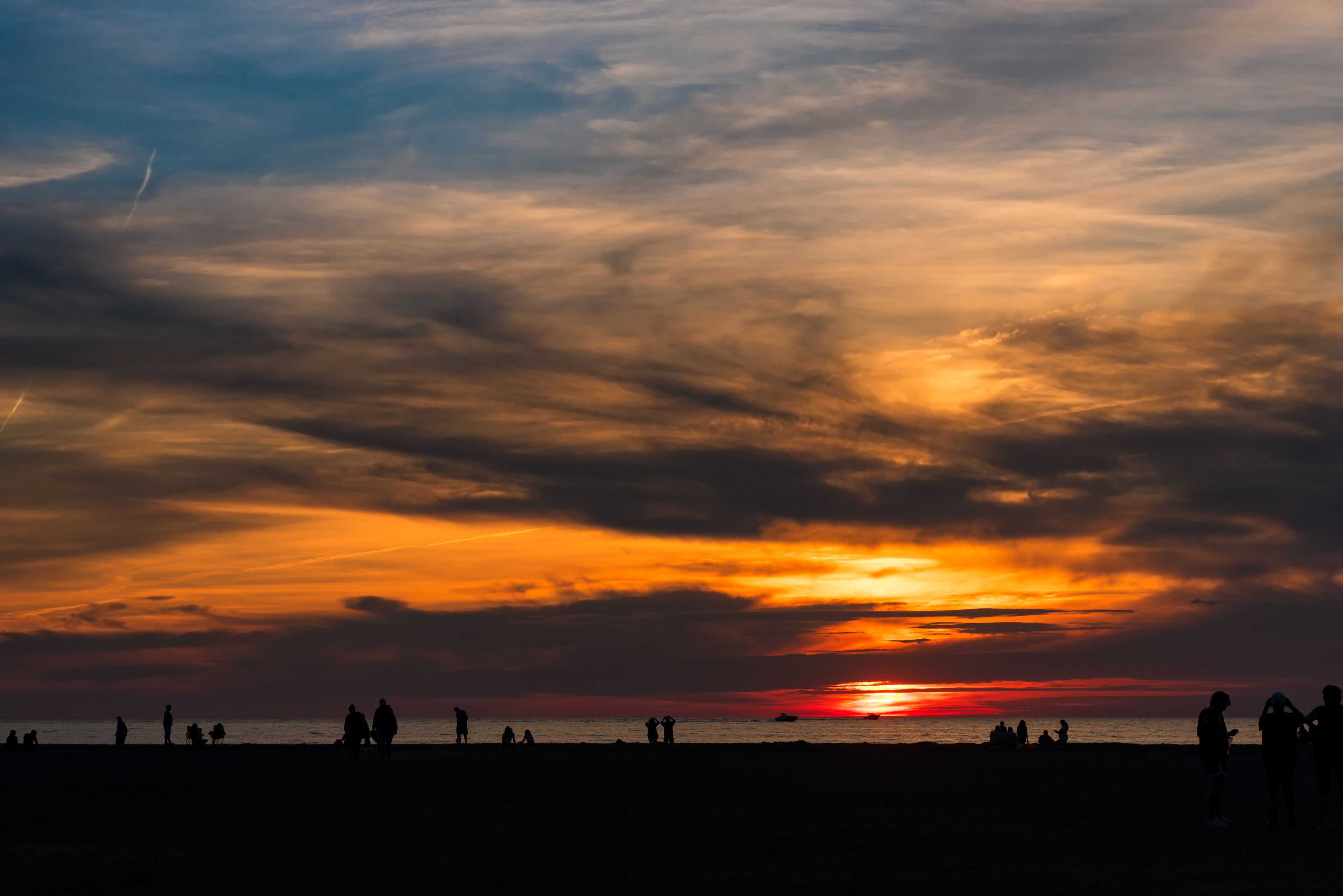 A sunset over a beach with silhouettes of people and a boat.