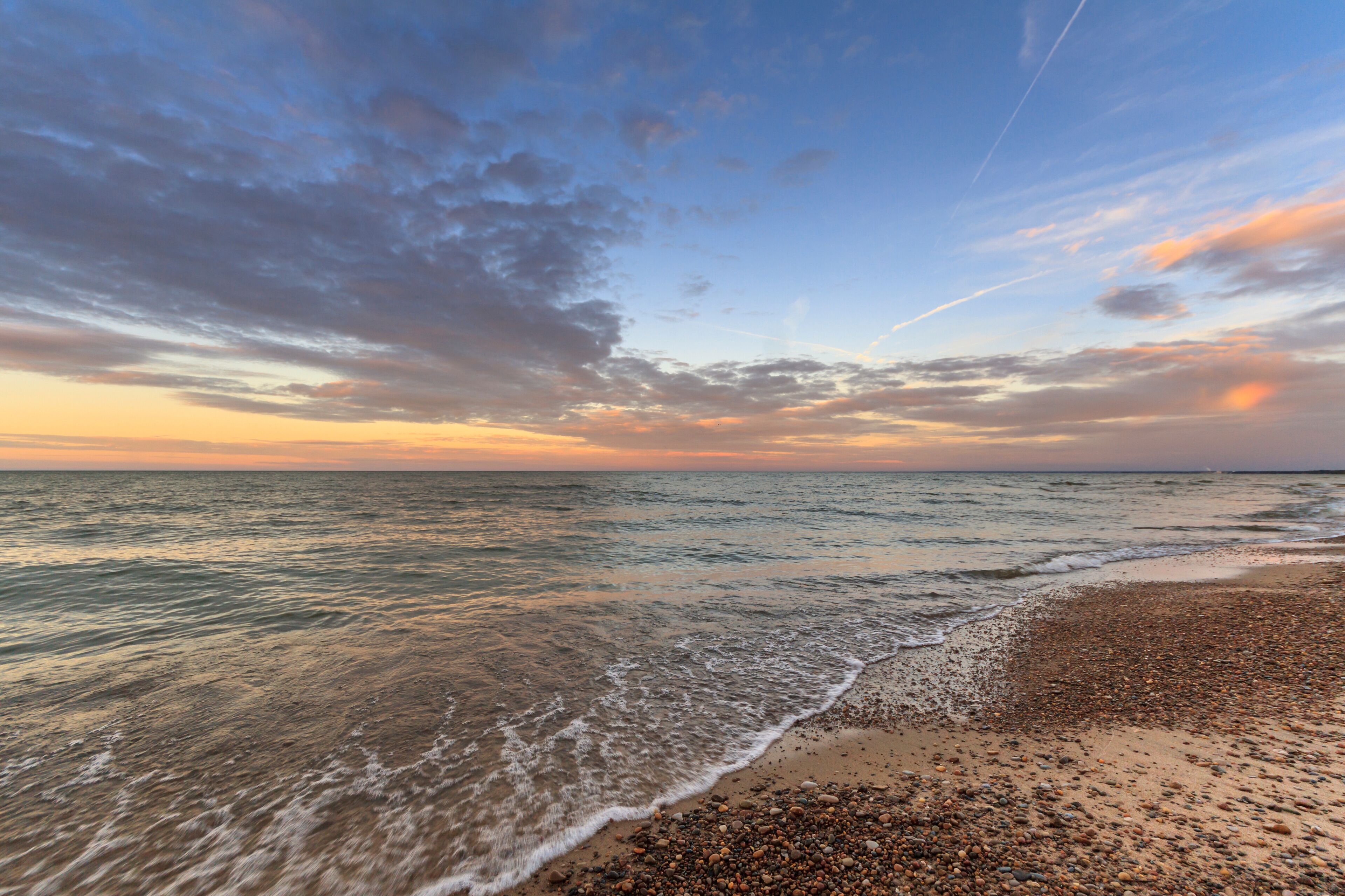 A beach with pebbles and waves at sunset.