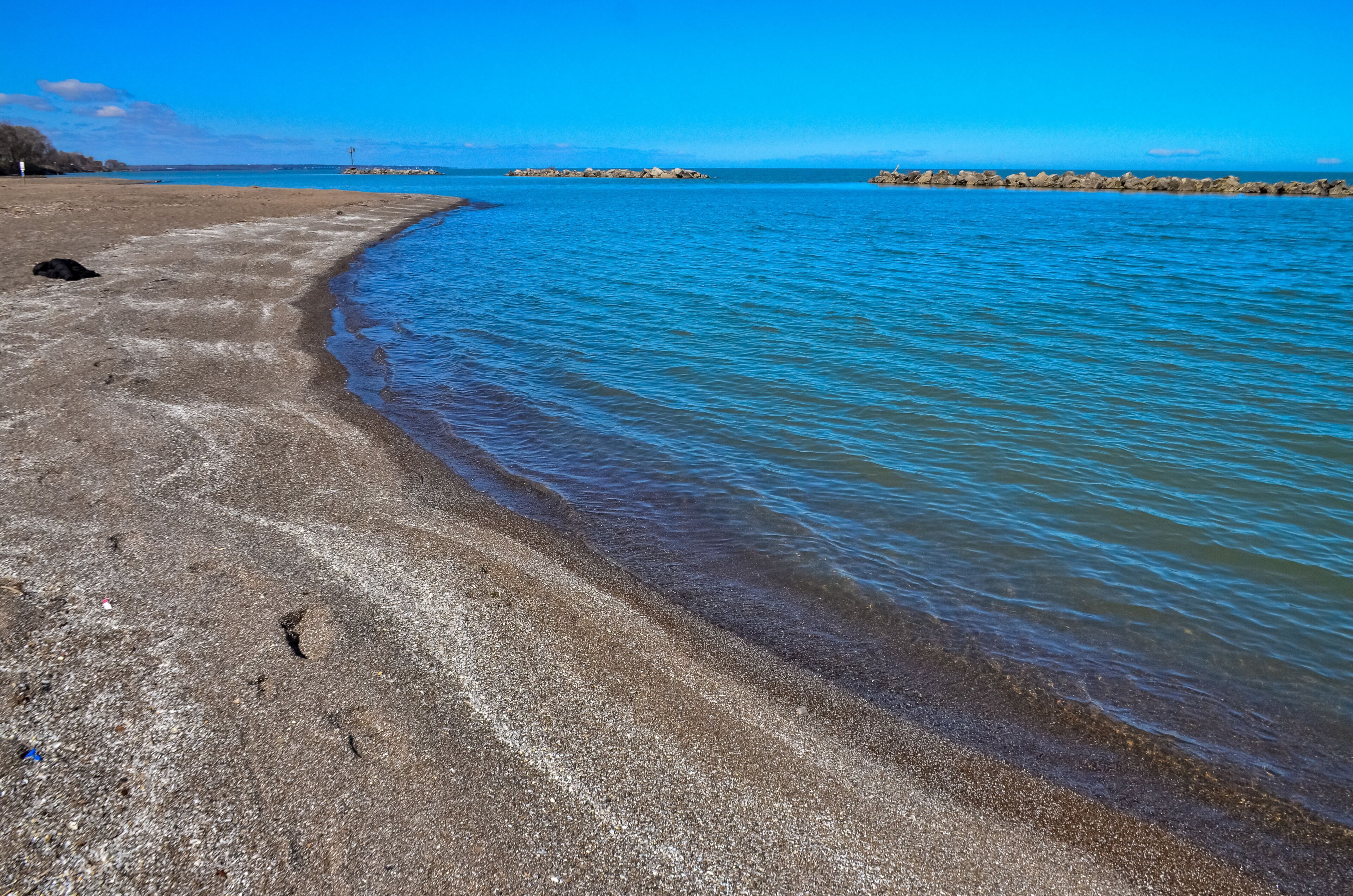 A beach with clear blue water, a sandy shore, and distant rocky outcrops.