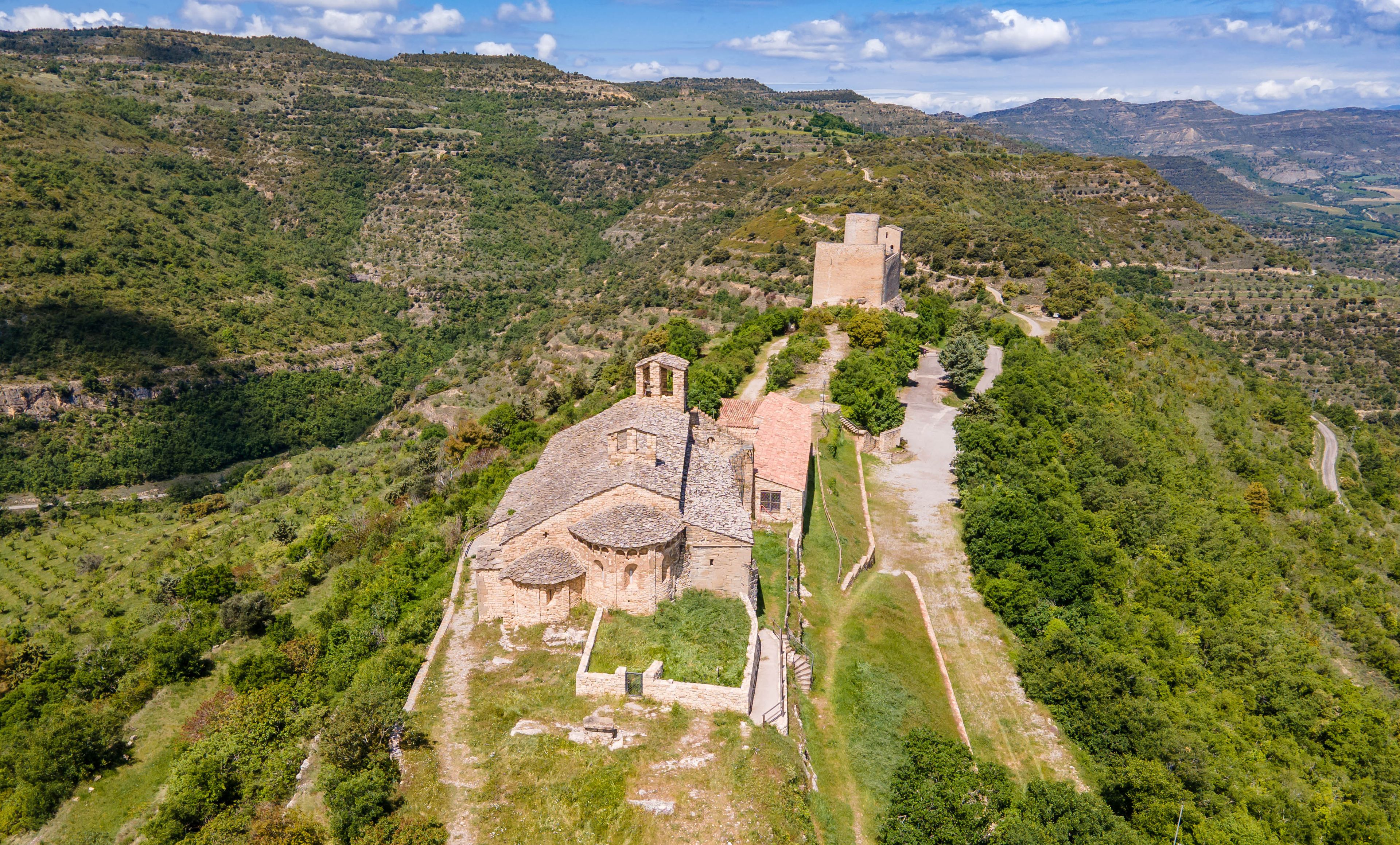 A historical church with a bell tower on a hillside, surrounded by lush greenery and a winding path.