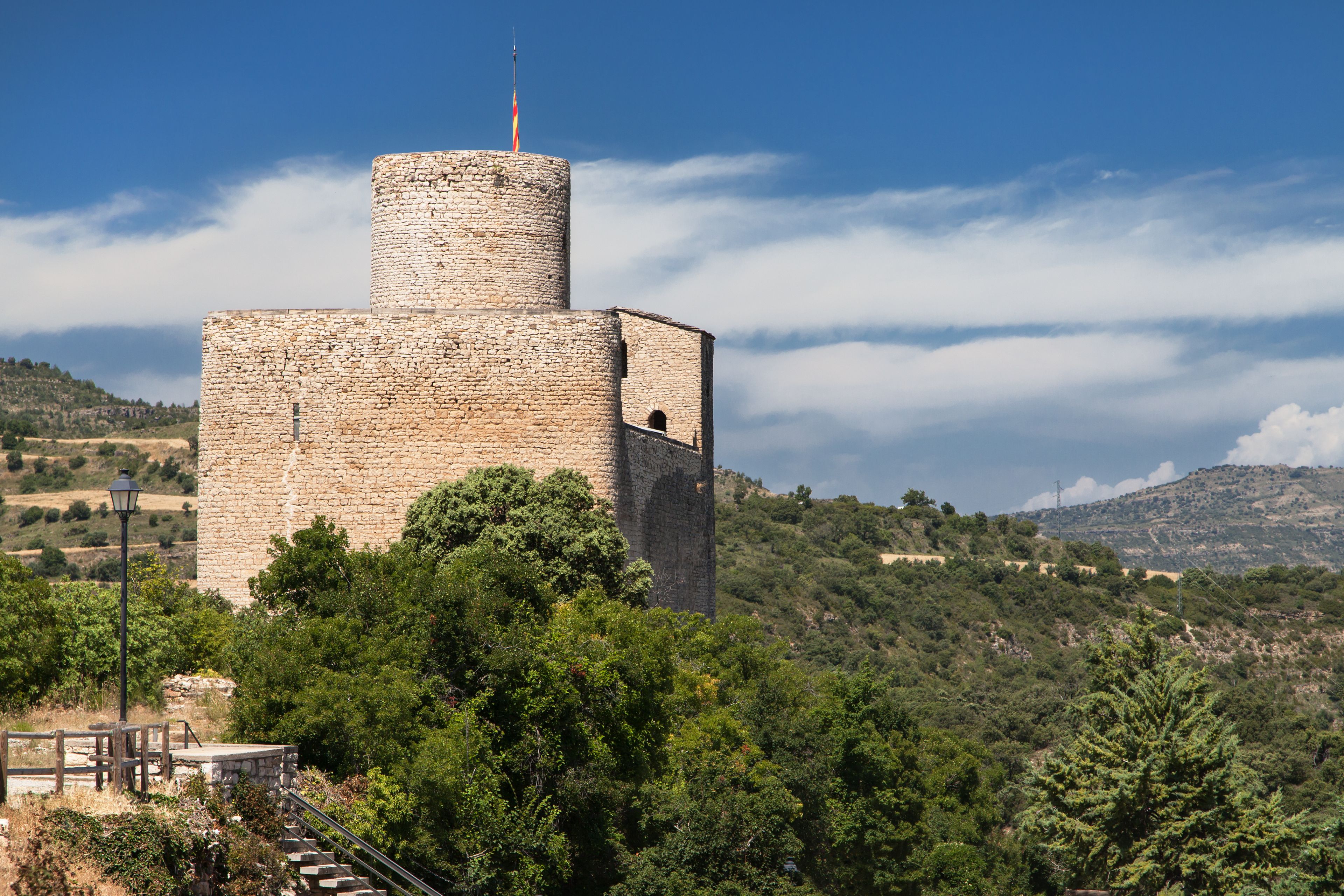 A stone tower with a flag on top, surrounded by lush greenery and hills in the background.