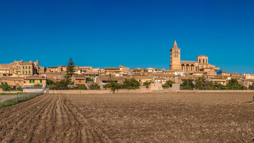 A town with a prominent church featuring a tall bell tower, surrounded by residential buildings and a large open field.