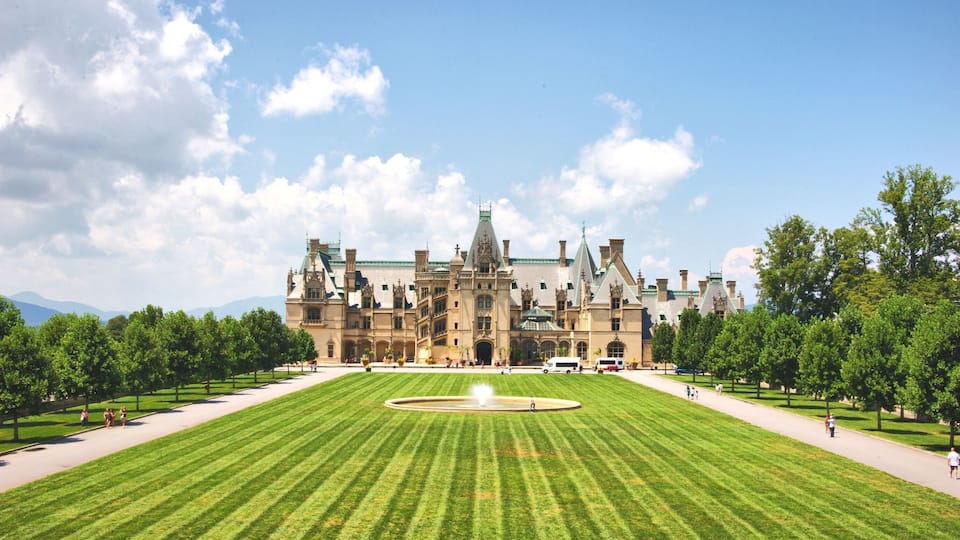 A large, historic building with a central fountain and a well-manicured lawn.
