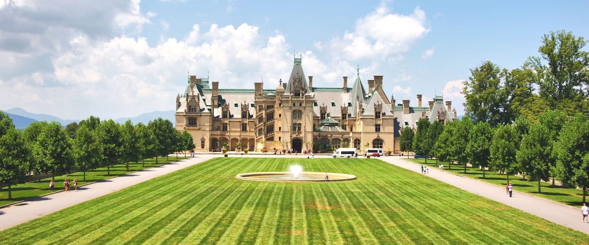 A large, historic building with a central fountain and a well-manicured lawn.