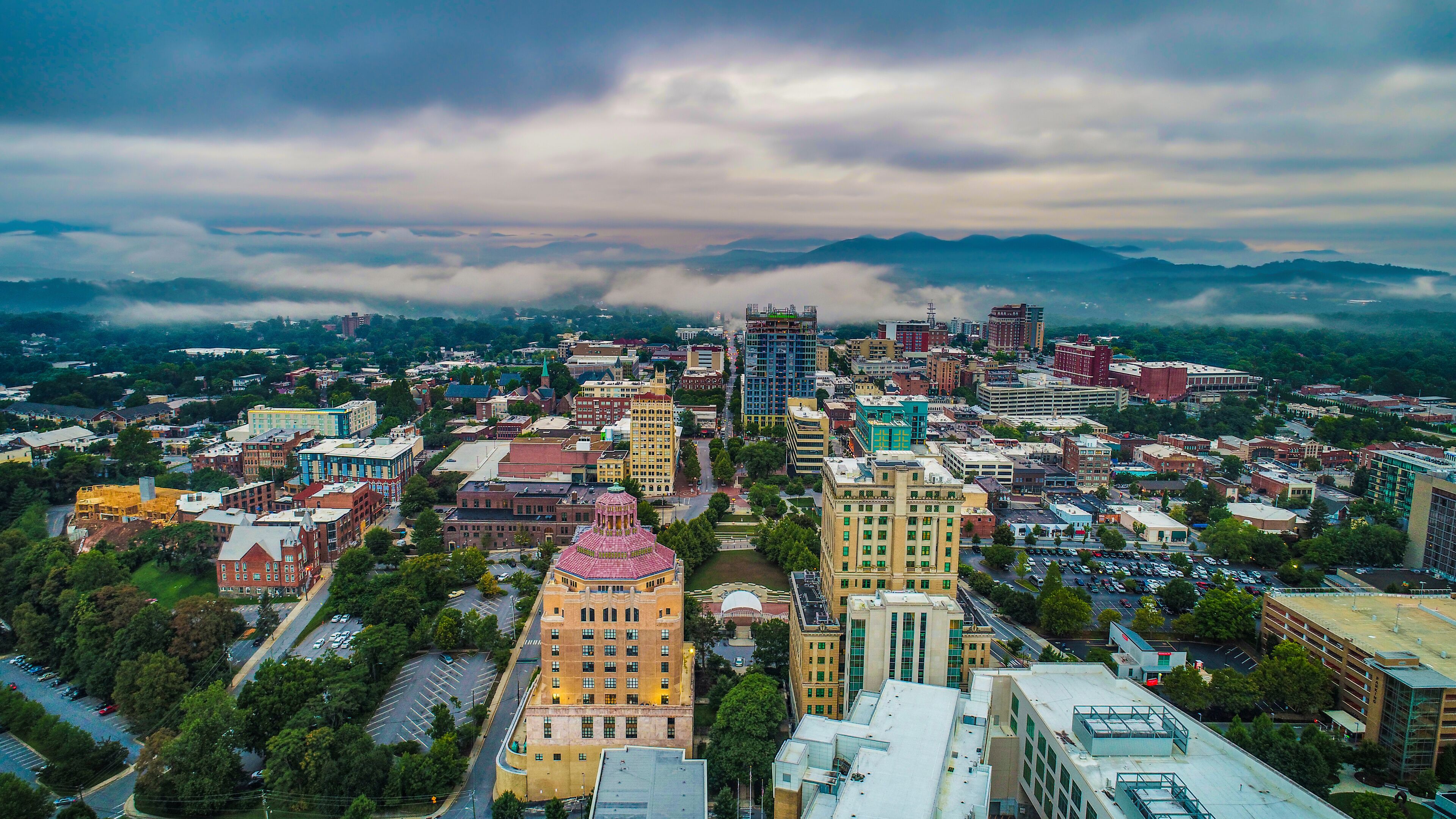 A cityscape with a mix of historic and modern buildings, a prominent dome structure, and a mountainous backdrop.