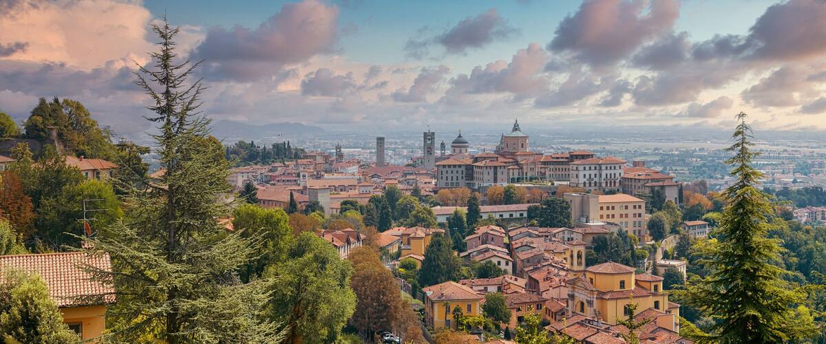 A panoramic view of a historic town with red-tiled roofs, surrounded by lush greenery and a clear sky.