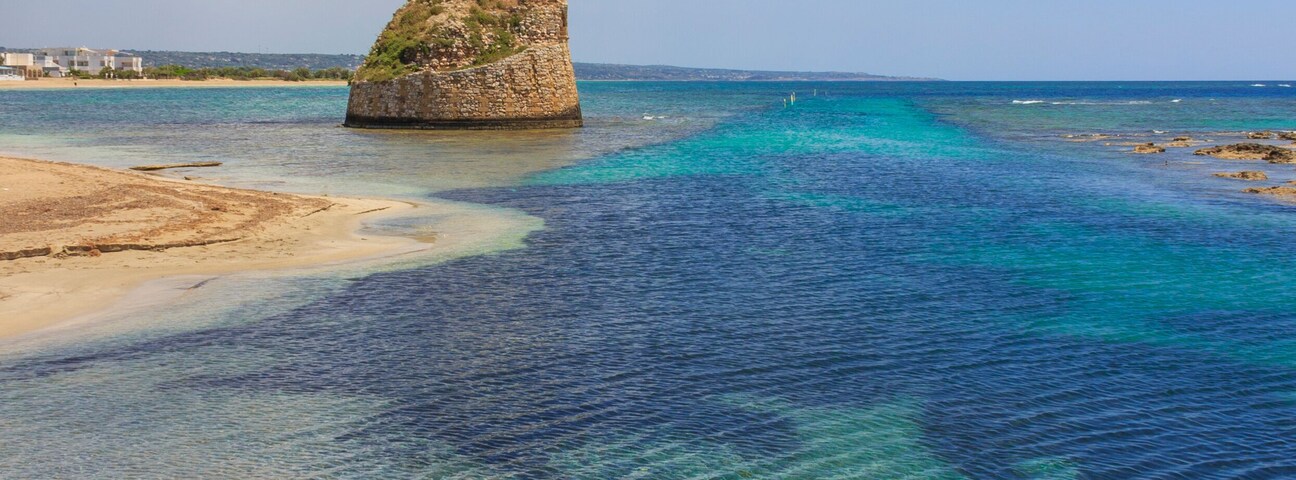 Un mar azul y transparente con una isla rocosa y una playa arenosa.