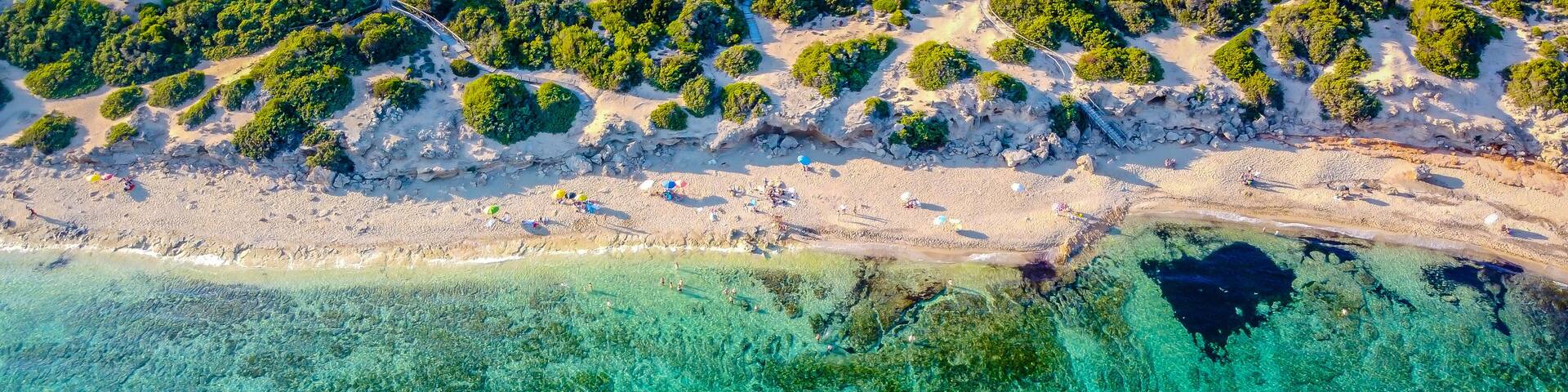 An aerial view of a beach with clear turquoise waters, sandy shore, and dense green vegetation.