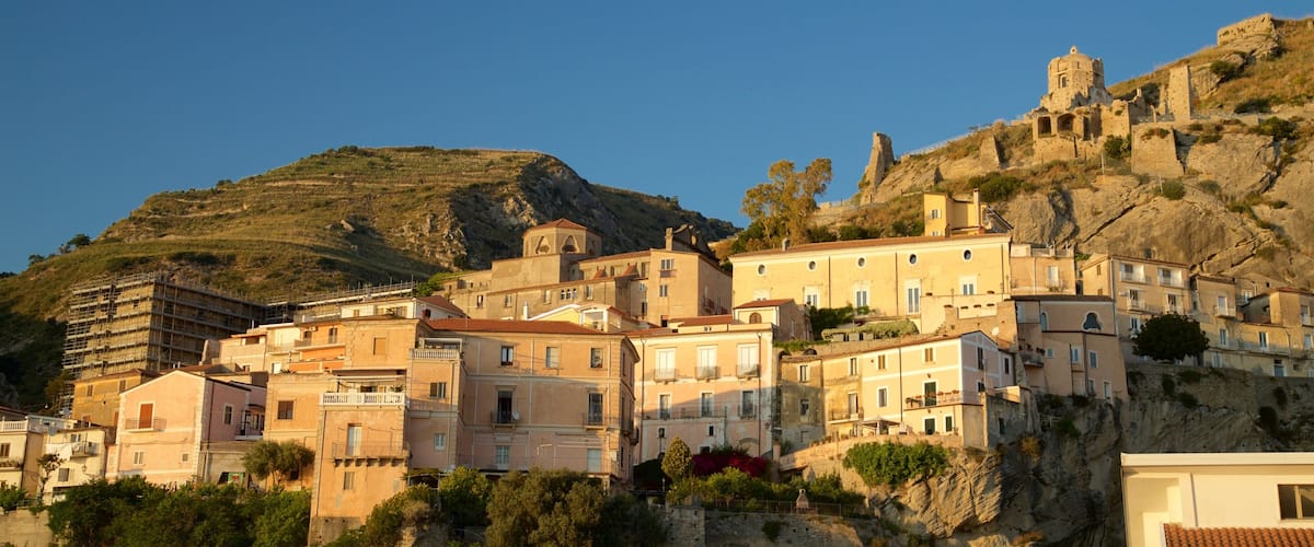 A coastal town with historic buildings perched on a hillside, a prominent church, and a rocky cliff in the background.