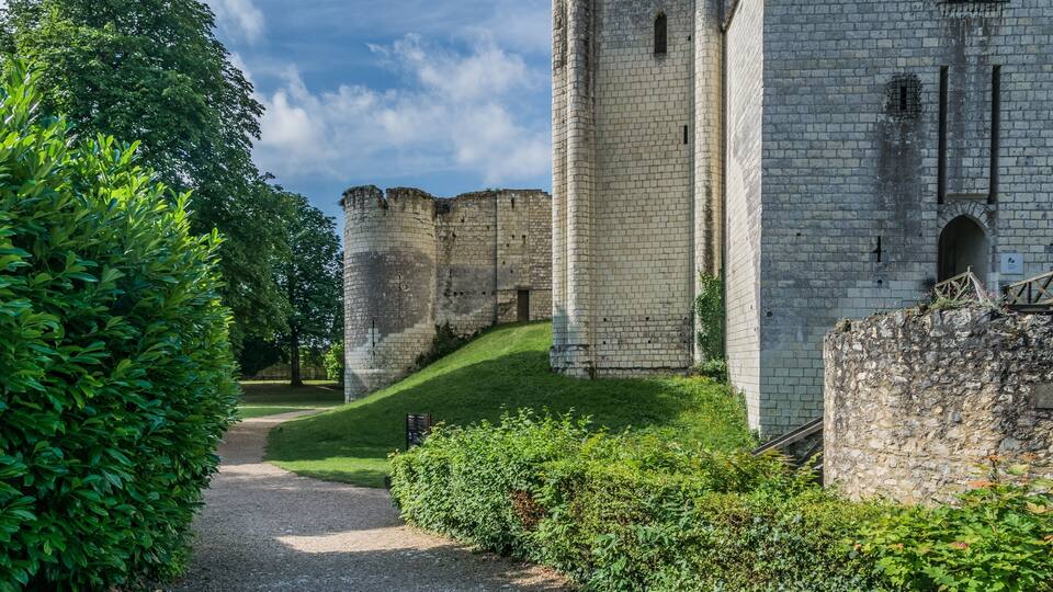A historic stone castle with a paved path leading to it, surrounded by lush greenery.