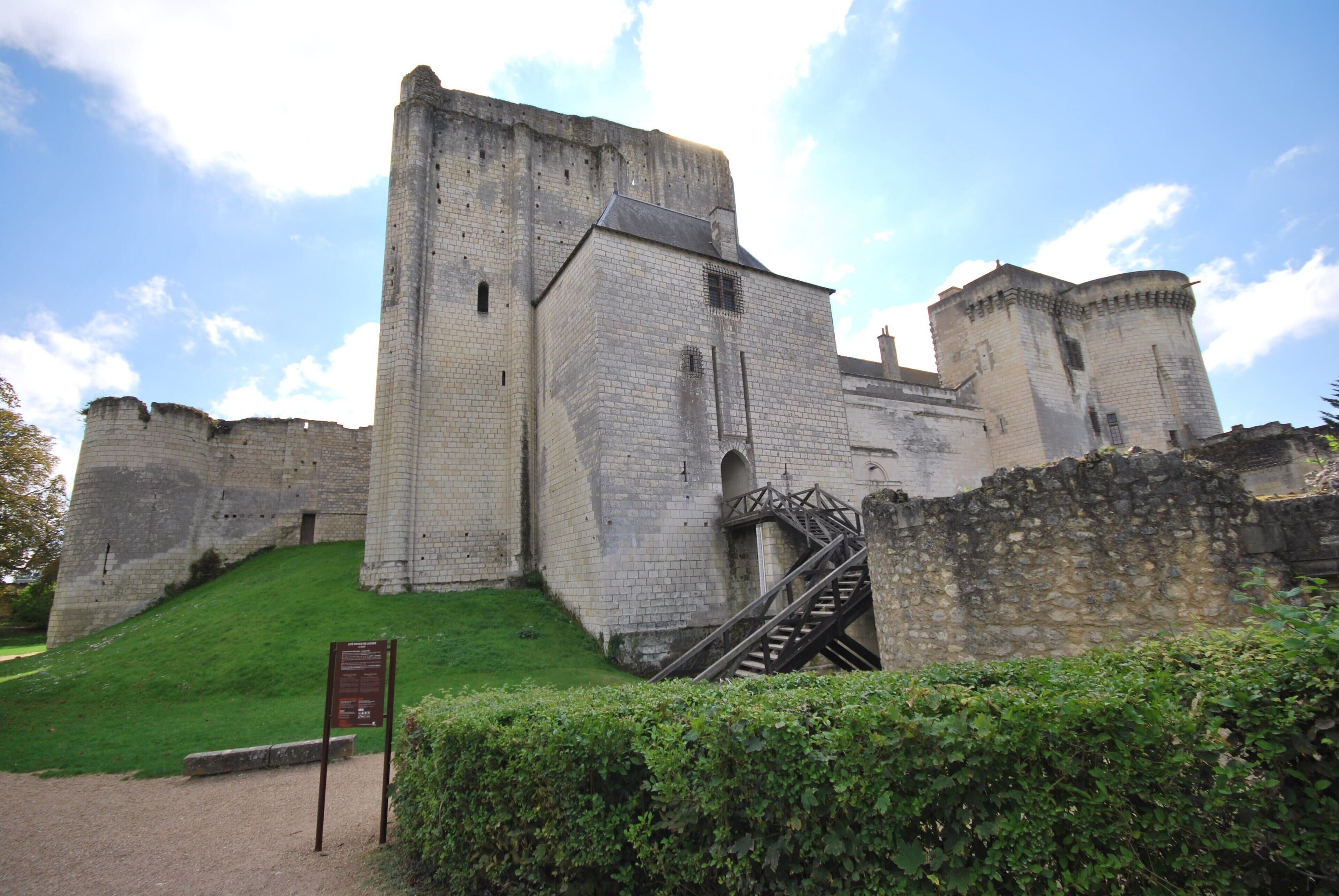 A historic stone castle with a large central tower, a staircase leading to the entrance, and a grassy hill in the foreground.