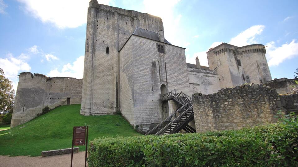 A historic stone castle with a large central tower, a staircase leading to the entrance, and a grassy hill in the foreground.