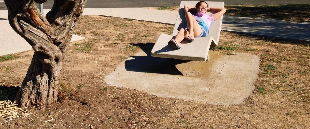 A person relaxing on a concrete bench in a park with a tree nearby.