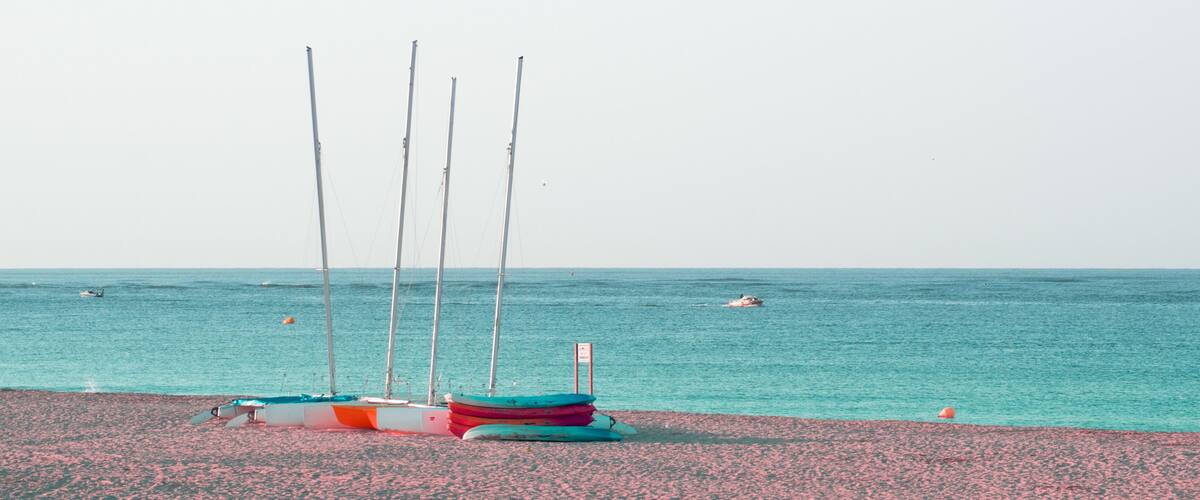 A beach with several colorful boats lined up and a few sailboats in the background.