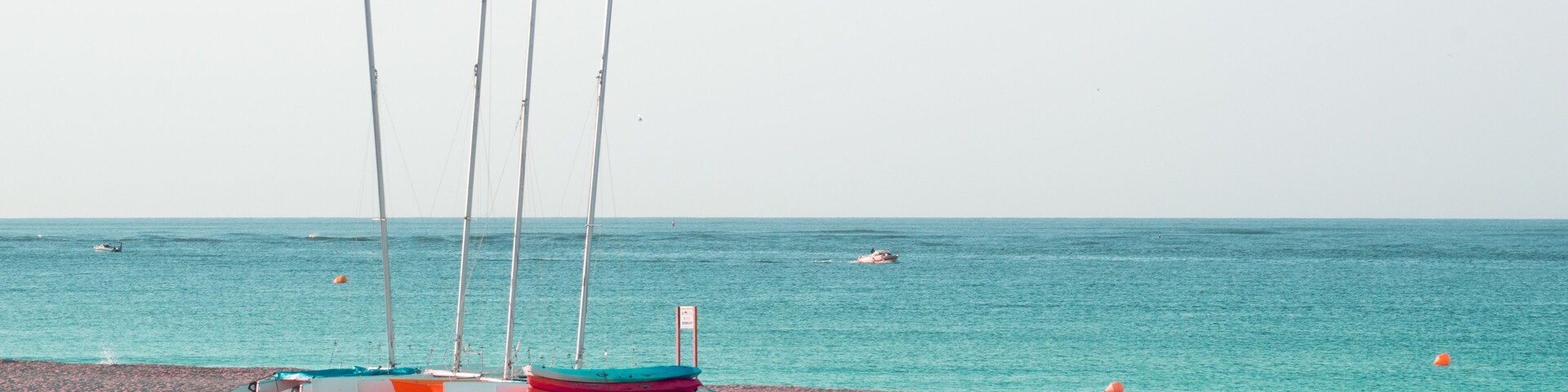 A beach with several colorful boats lined up and a few sailboats in the background.