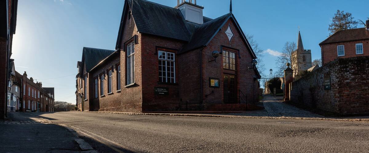 A historic brick building with a bell tower, a cobblestone street, and a church in the background.