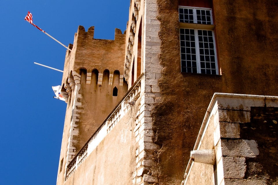 A historic stone castle with battlements, a flagpole, and a window.