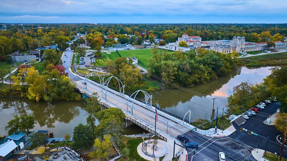 A bridge over a river, surrounded by autumn foliage and a town with historic buildings.