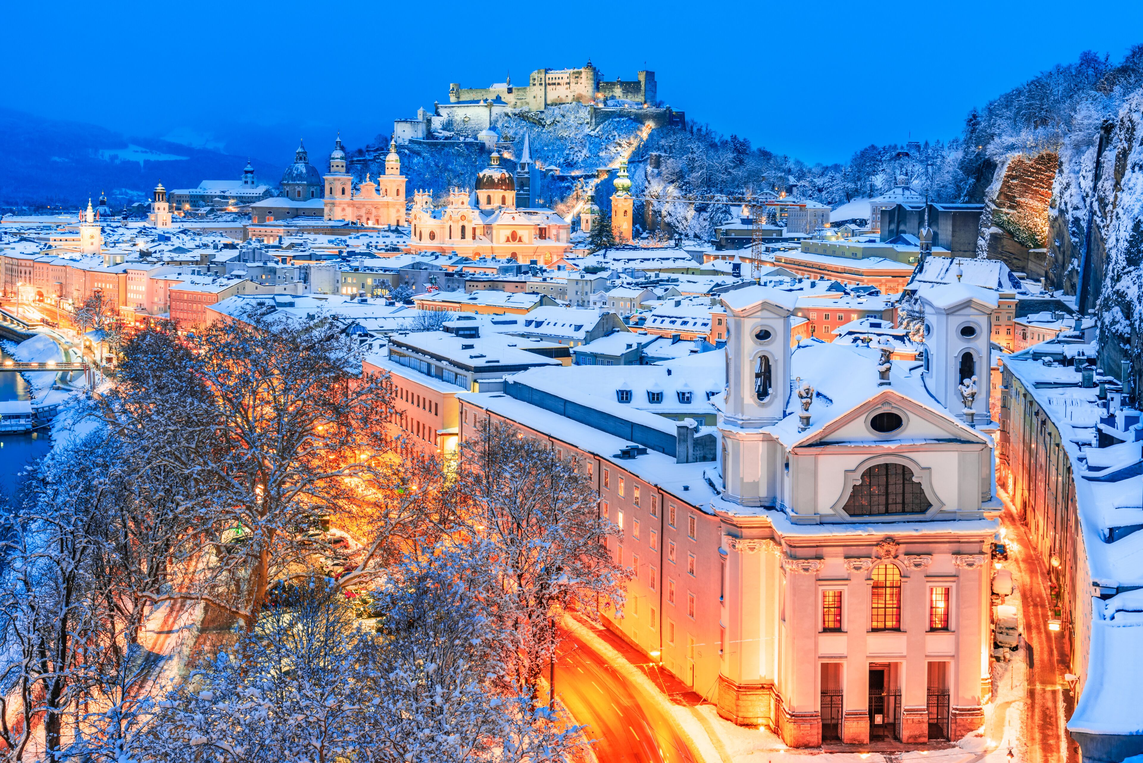 A snow-covered cityscape with historic buildings and a castle on a hill.