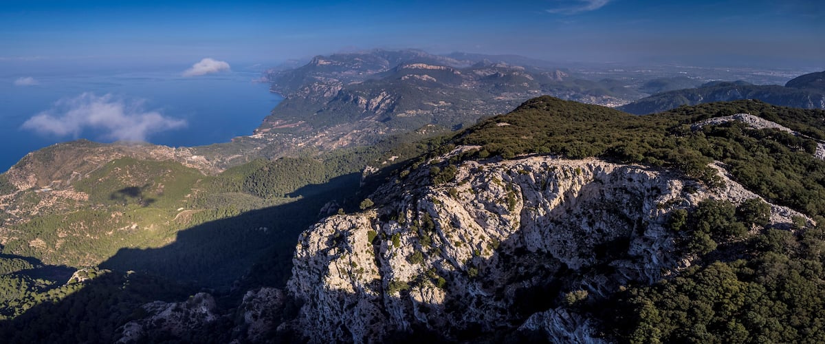 A mountainous landscape with a coastal view, rocky cliffs, and dense forests.