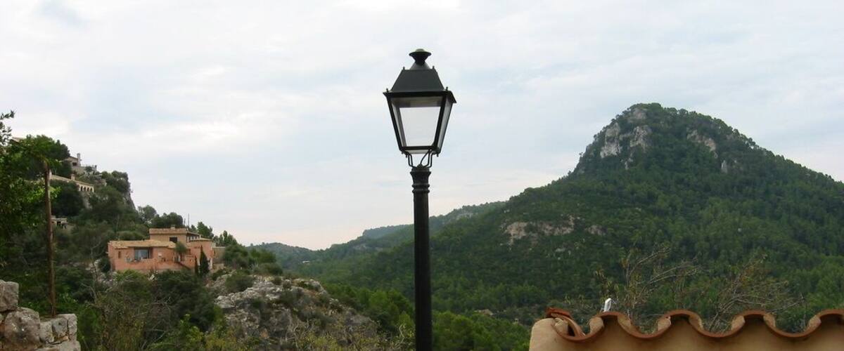 A mountain landscape with a traditional lamp post and terracotta-roofed structures.