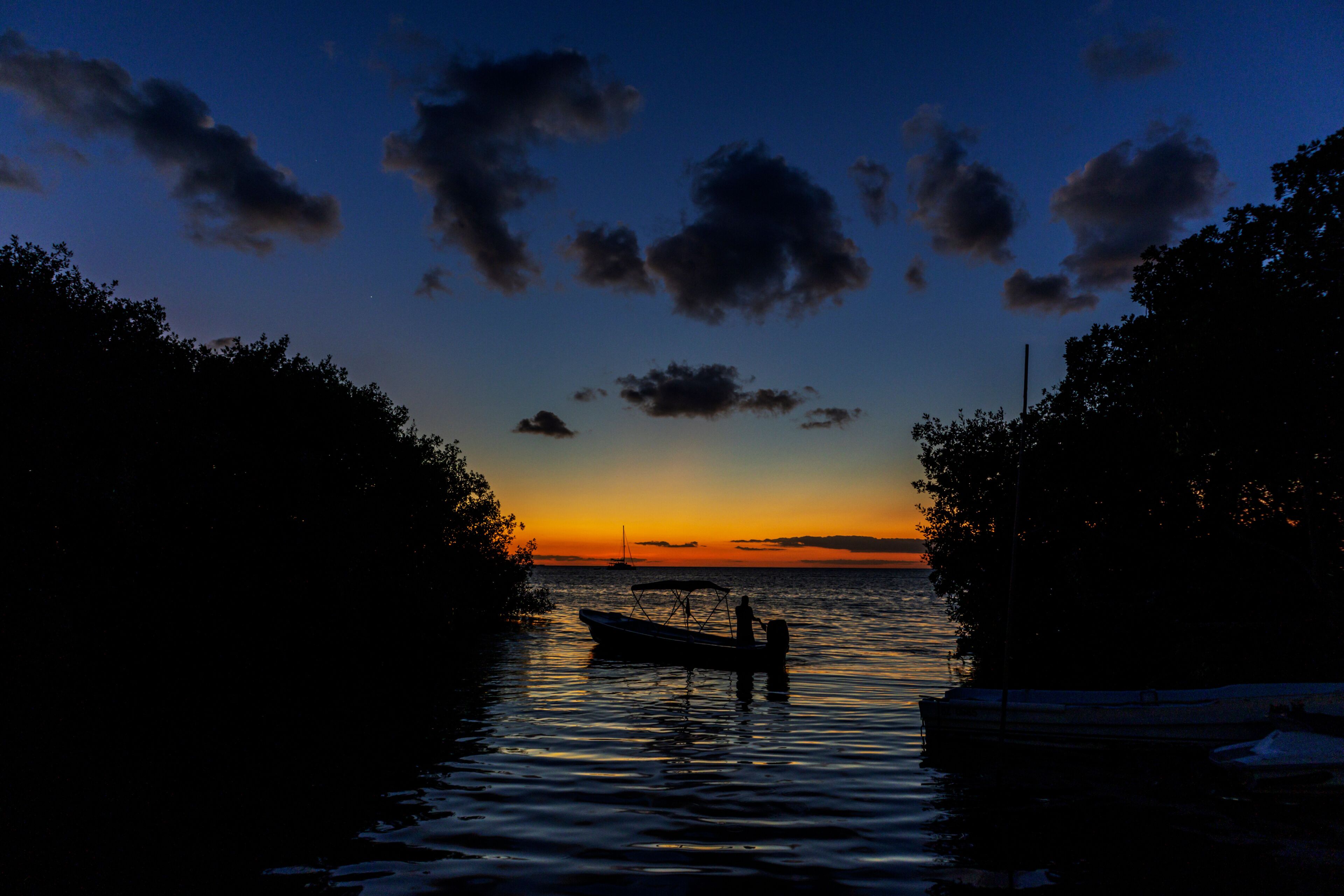 Um pôr do sol sobre águas calmas, com um barco ancorado ao centro, cercado por árvores.